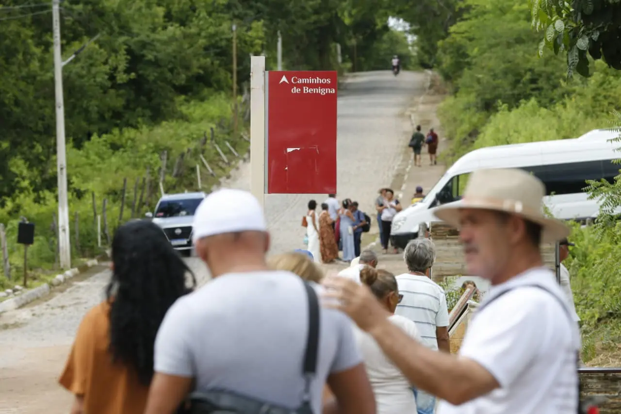 Turistas caminhando pela trilha de Caminhos de Benignga com sinalização e vegetação ao redor.