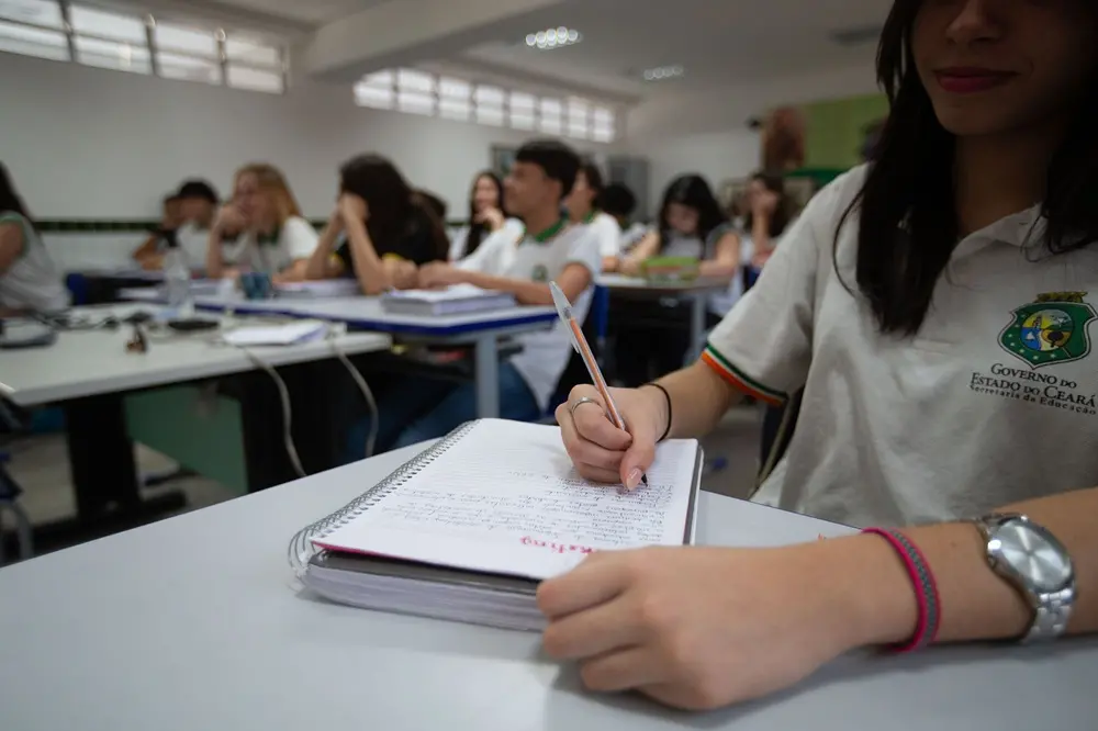 imagem de alunos na sala de aula, com foco em uma aluna escrevendo em uma caderno.