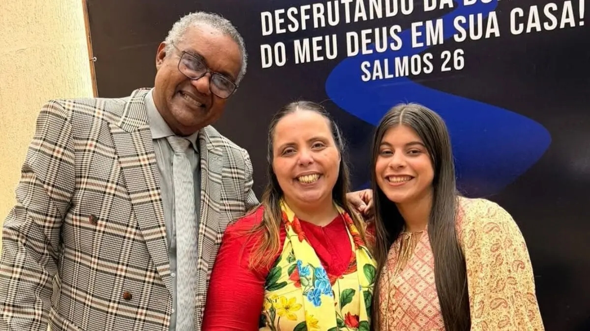Três pessoas sorridentes em evento religioso, com destaque para uma mulher vestida de vermelho e criança ao lado, em ambiente de celebração cristã.
