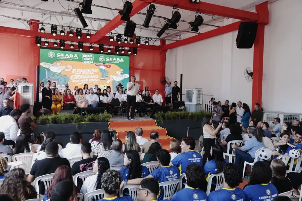 imagem de um evento com um palco e a plateia e o governador Elmano de Freitas falando ao microfone