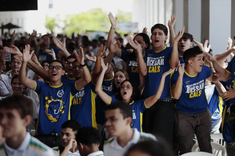 estudantes com braços erguidos enquanto cantam uma música em referência à escola.