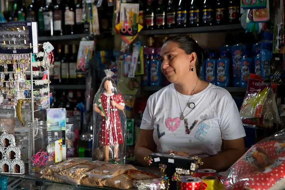 Na imagem, fotografia em plano médio de uma mulher de cabelos presos e camiseta branca com a palavra 