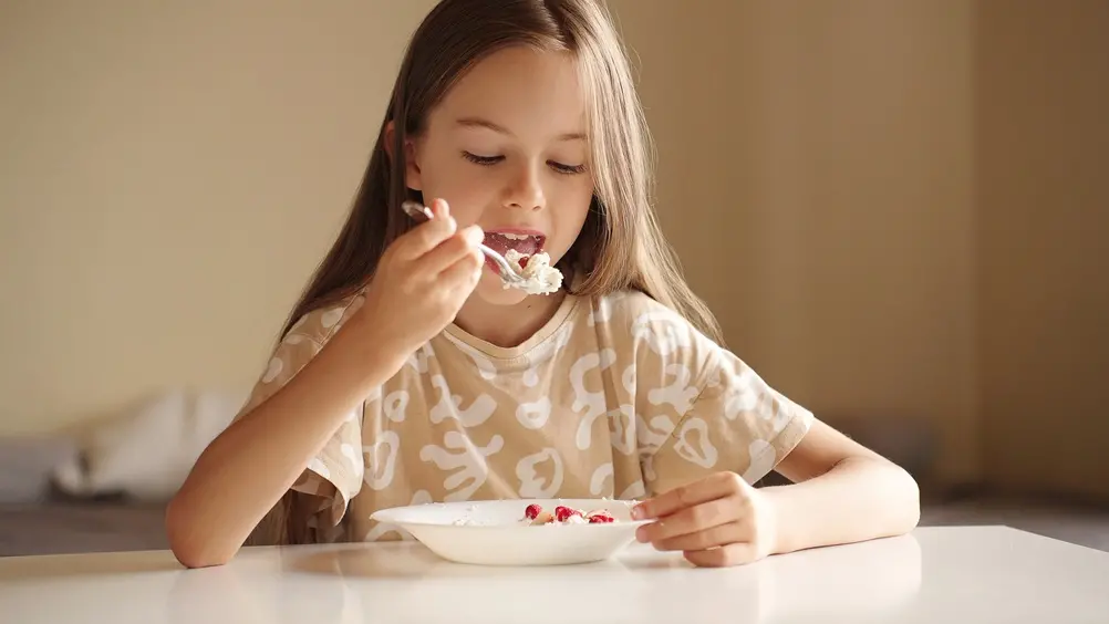 foto de menina comendo fruta e cereais em prato branco.