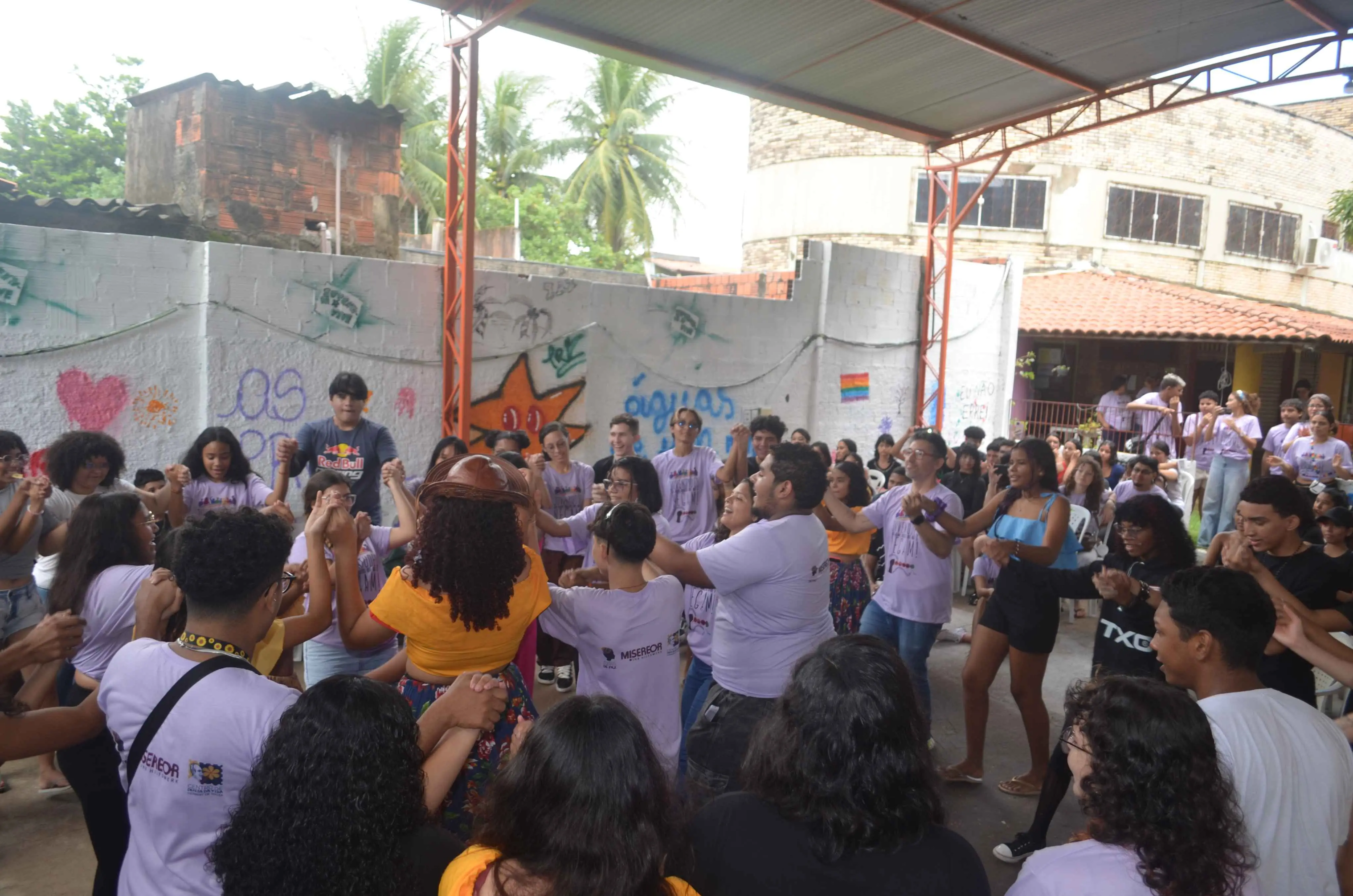Grande grupo de jovens de mãos dadas forma uma roda em pátio coberto com paredes grafitadas, durante atividade do Centro de Defesa da Vida Herbert de Souza.