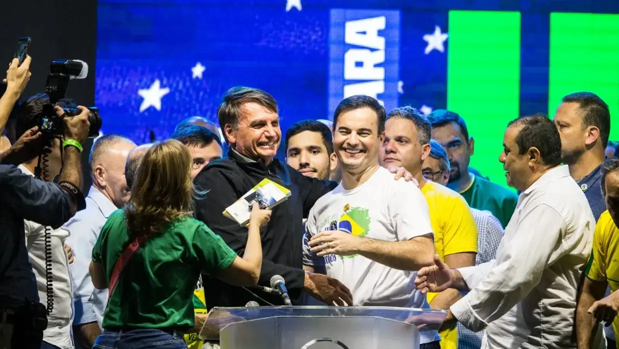 O ex-presidente Jair Bolsonaro aparece ao lado de Capitão Wagner em palco durante evento político, cercado por apoiadores e pessoas vestidas com cores da bandeira do Brasil.