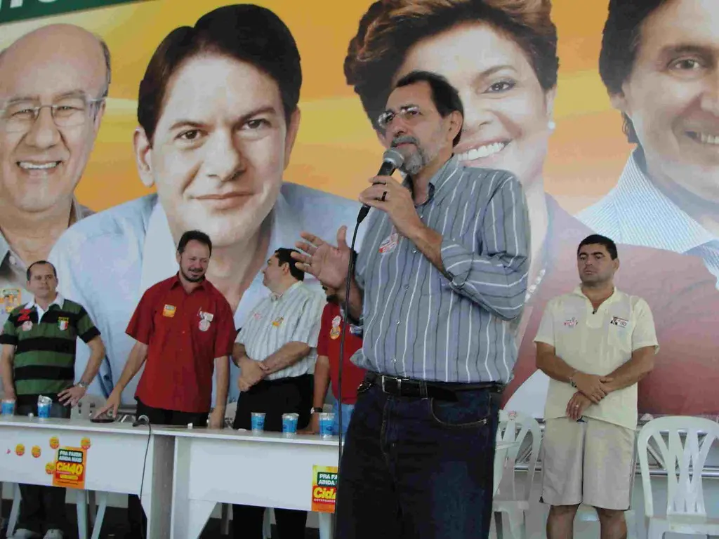 Professor Pinheiro discursa e gesticula durante plenária do PT. Atrás dele, uma mesa com aliados o escutam.