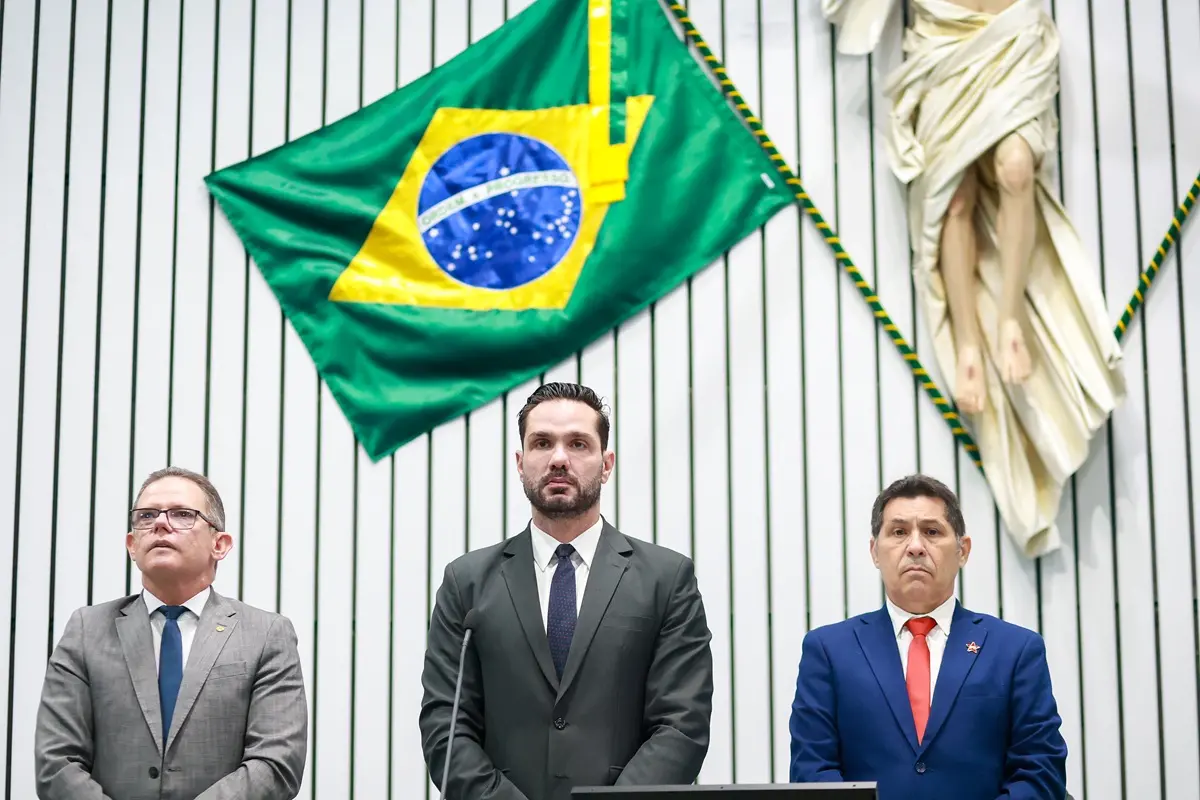 Três deputados em pé, à frente de bandeira do Brasil, na Assembleia Legislativa do Ceará.