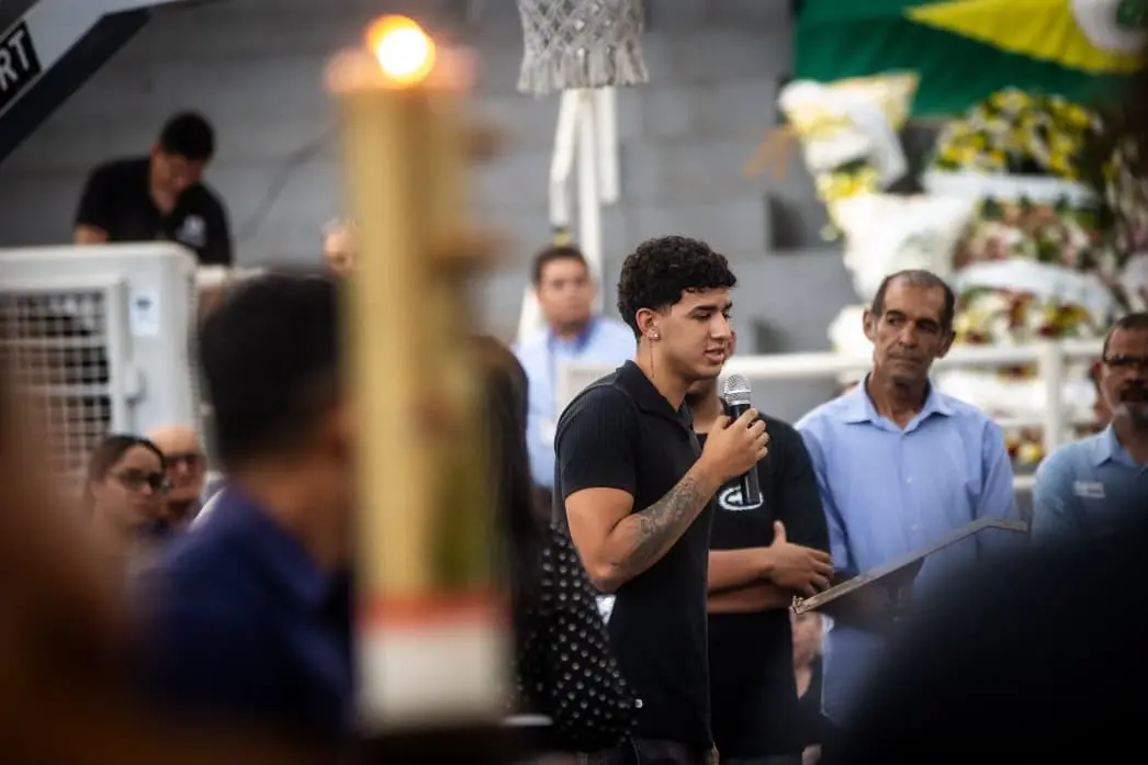 Foto mostra jovem de camisa preta discursando no velório de vítimas.