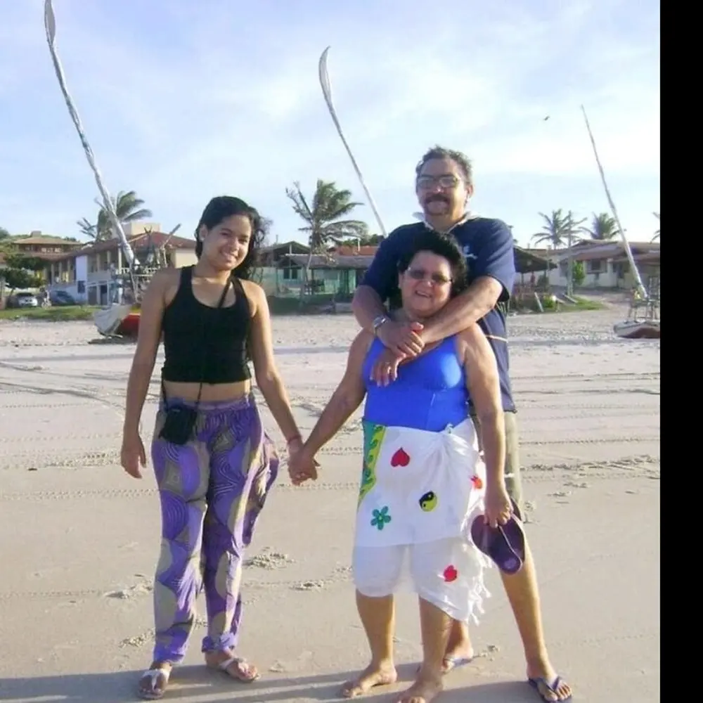Na imagem, uma foto ao ar livre, colorida e de plano médio, sob a luz do sol brilhante na areia da praia, mostrando o Seu França e familiares (conforme o nome do arquivo 
