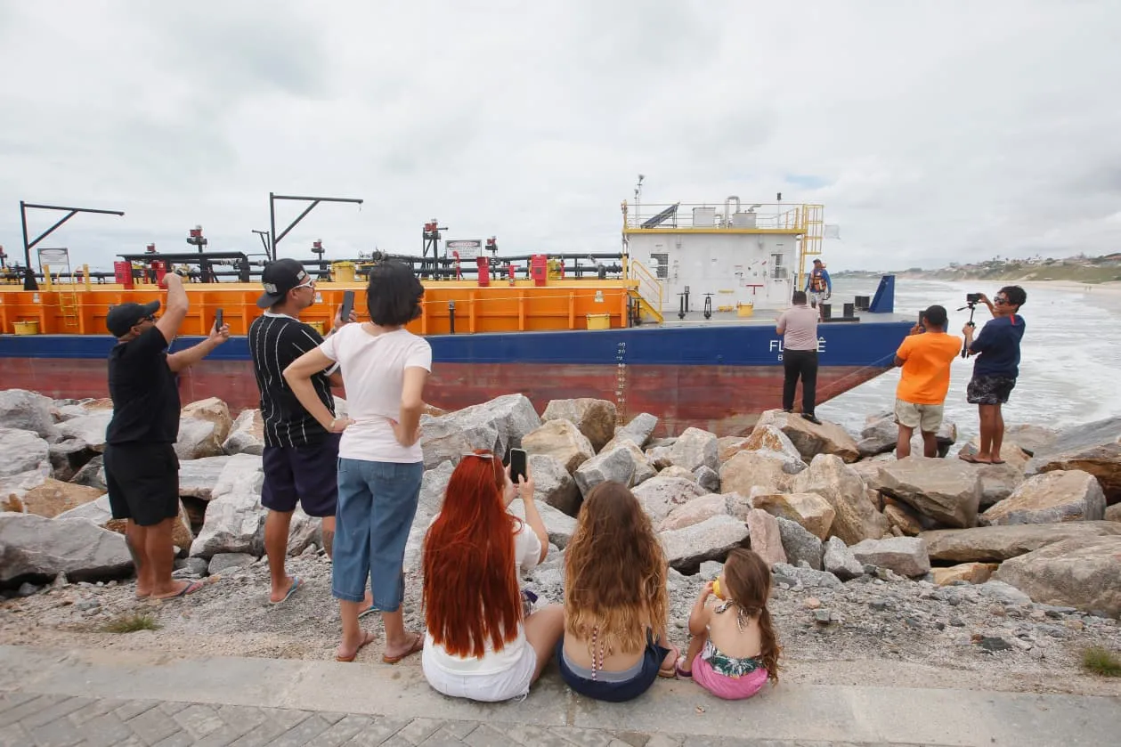 Na faixa de rochas da praia, pessoas registravam com celulares a grande balsa encalhada próxima à costa.